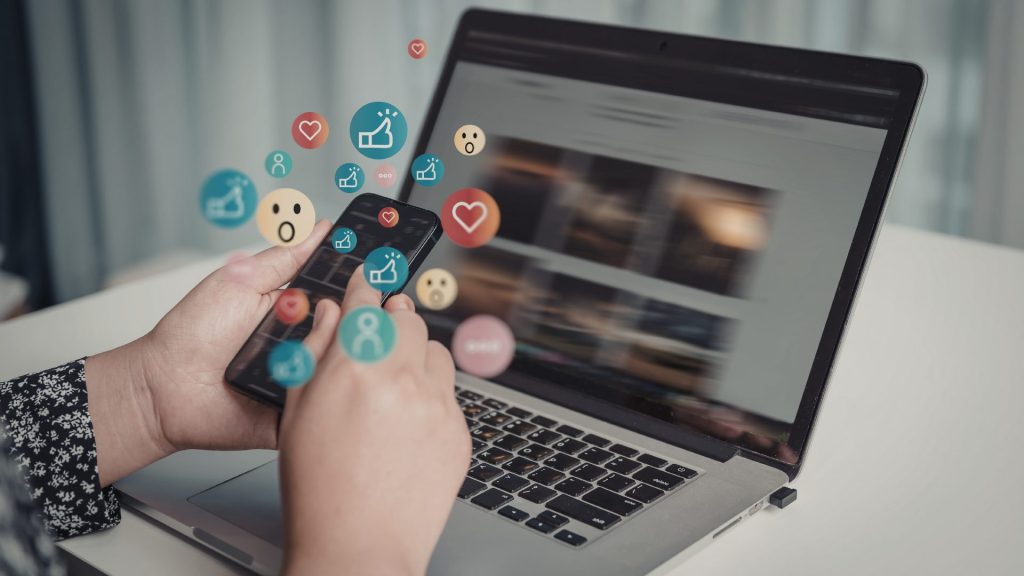 Personne qui tape sur un ordinateur portable entourée d'icônes de réseaux sociaux pour illustrer une stratégie de recyclage de contenu