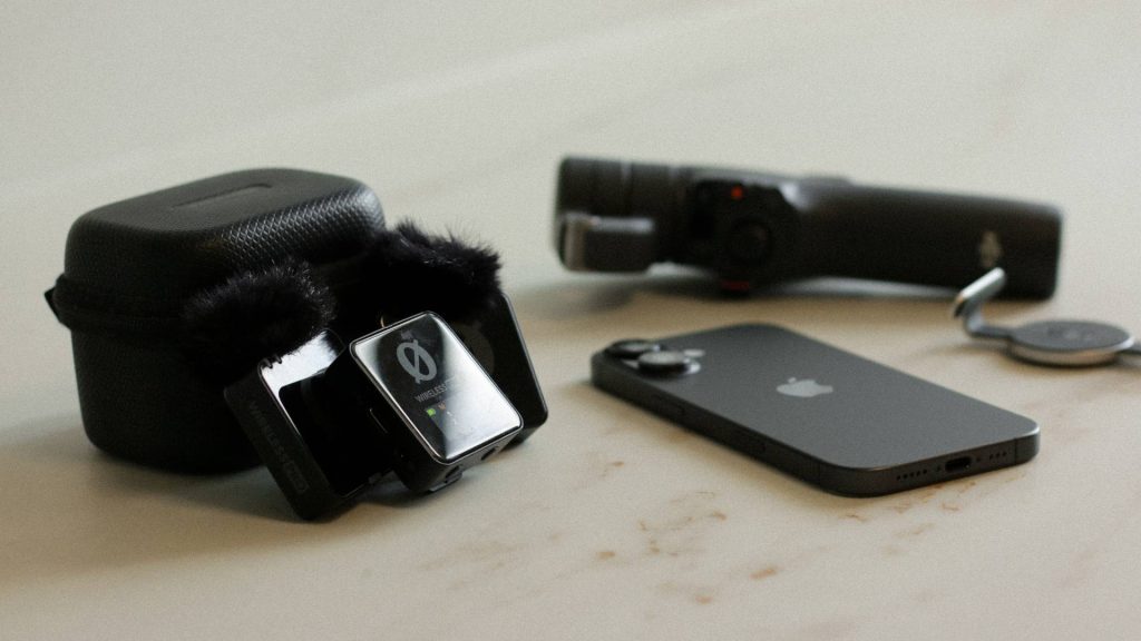 Équipement de tournage mobile agile sur une table, incluant un iPhone noir, un boîtier et des microphones sans fil RØDE avec bonnettes anti-vent, ainsi qu'un stabilisateur pour smartphone. Ce matériel est utilisé par l'équipe d'Effet-B à Saint-Sauveur pour la création de contenu vidéo authentique et performant.